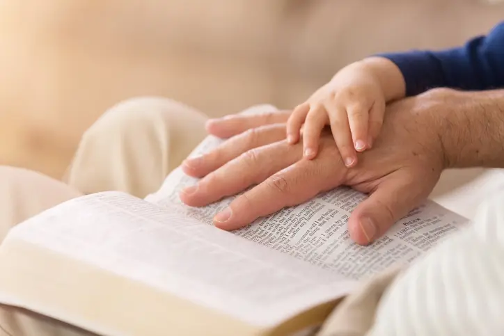 Child's hand on adult's hand over an open book