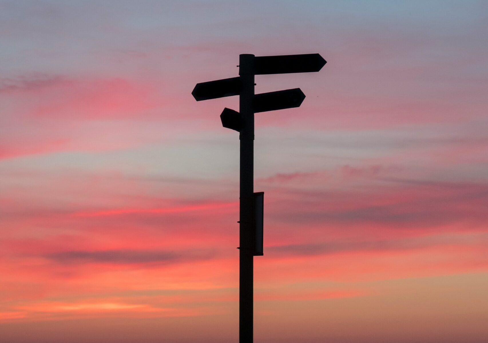 Silhouetted directional signpost against sunset sky