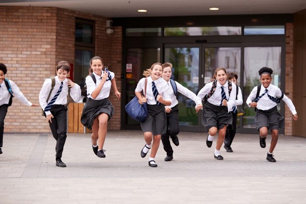 Cheerful children rushing out of school in uniforms