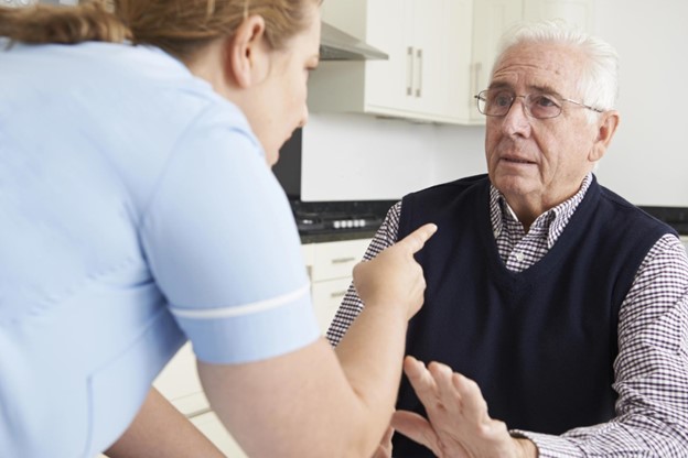 Elderly man discussing with female nurse in kitchen.