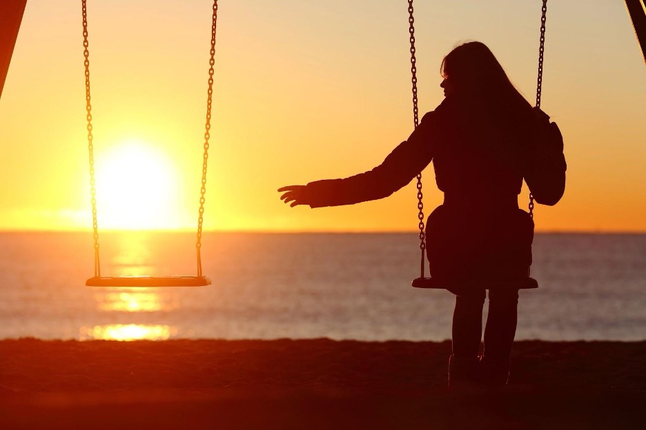 Silhouette of woman on swing at sunset by sea